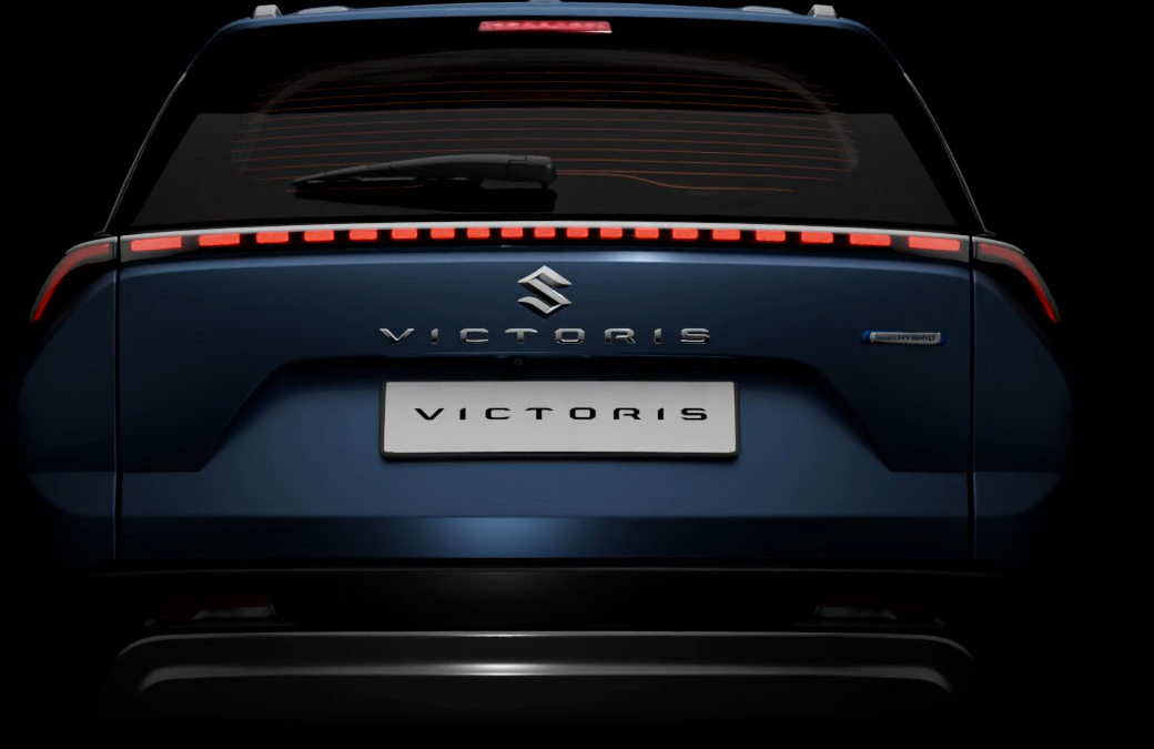 Rear view of the Maruti Suzuki Victoris showcasing its sleek LED tail light bar, Victoris badge, and hybrid emblem on a dark blue exterior.