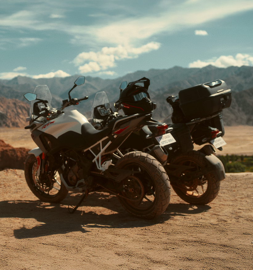 Two TVS Apache RTX 300 adventure motorcycles parked on a scenic mountain trail, equipped with touring boxes and helmets, ready for a long-distance ride.