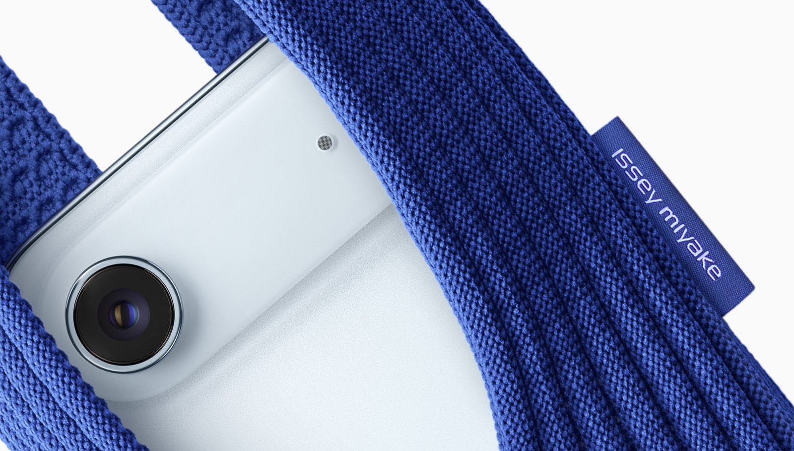 Close-up of an Apple iPhone partially enclosed in a blue Issey Miyake–designed knitted iPhone Pocket, highlighting the camera lens and fabric texture.