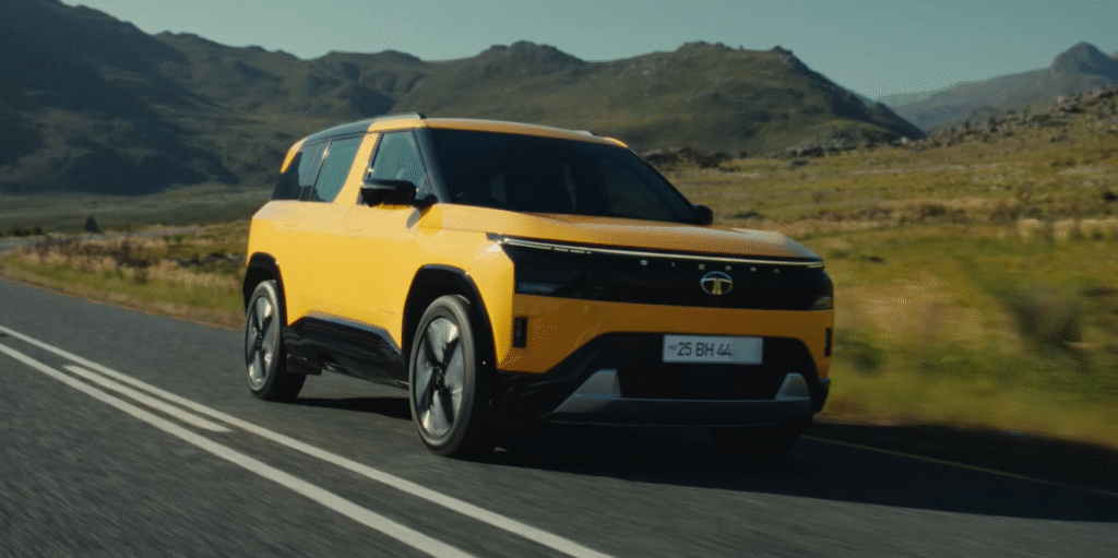 Tata Sierra 2025 in yellow driving on an open highway with mountains in the background, showcasing its futuristic front design and strong road presence.