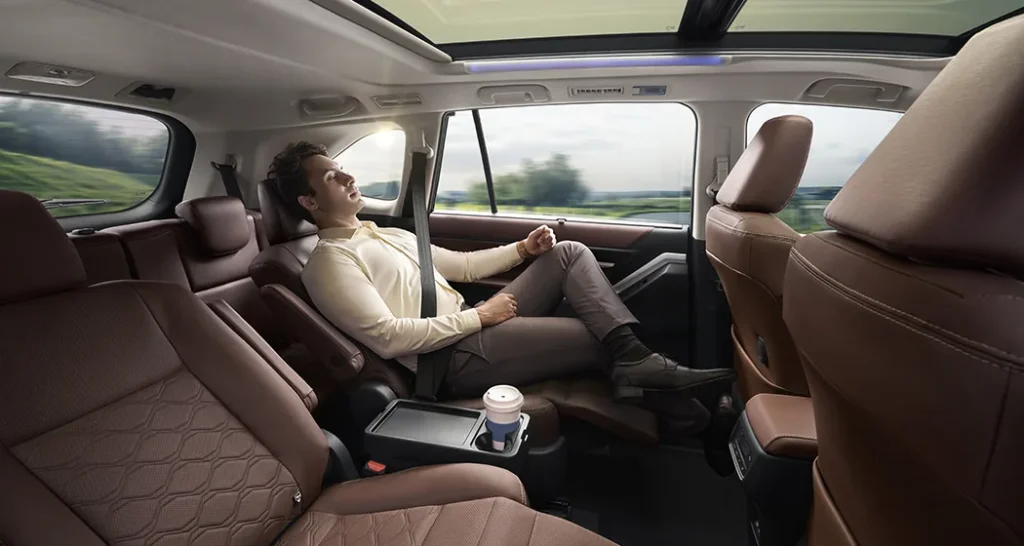 Toyota Innova HyCross interior with a passenger relaxing in the second-row captain seat, showcasing luxurious brown leather upholstery, panoramic sunroof, and spacious comfort.